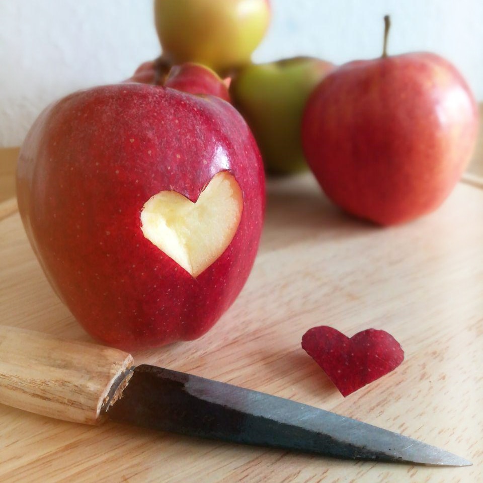Ein Apfel in den ein Herz geschnitzt wurde. Davor ein kleines Messer.