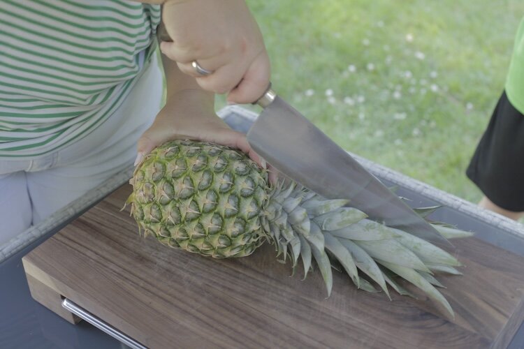 Frau schneidet mit Kochmesser eine Ananas