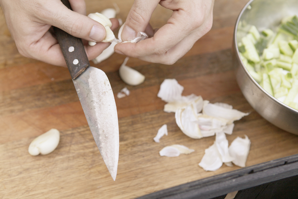 Person zerkleinert Knoblauch mit einem Authentic Blades Messer auf einem Holzschneidebrett